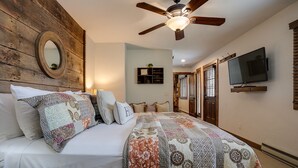 A bedroom with a wooden headboard, a ceiling fan, a bed with a floral quilt, a wall clock, and a television mounted on the wall. - NLTH3 | Mountain Living | Ski Out/Walk In | Winter Shuttle | Hot Tub (Steamboat Springs)