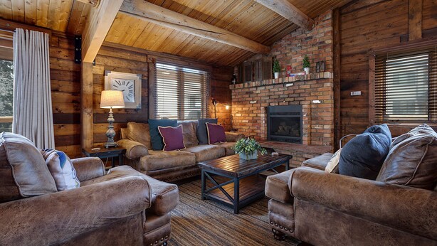 A cozy log cabin interior with a fireplace, leather sofas, and a rustic wooden ceiling. - NLTH3 | Mountain Living | Ski Out/Walk In | Winter Shuttle | Hot Tub (Steamboat Springs)