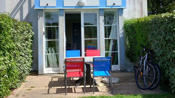 Una casa de dos pisos con un balcón, una puerta principal y un pequeño patio con sillas y una mesa.