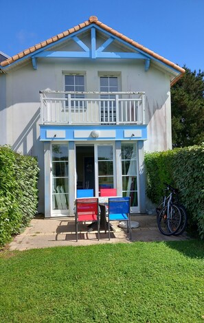 A two-story house with a balcony, a front door, and a small patio area with chairs and a table.