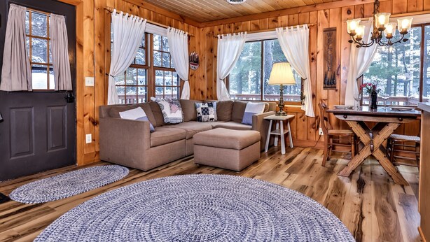 A cozy cabin interior with a wooden interior, a sofa, a dining table, and a chandelier.