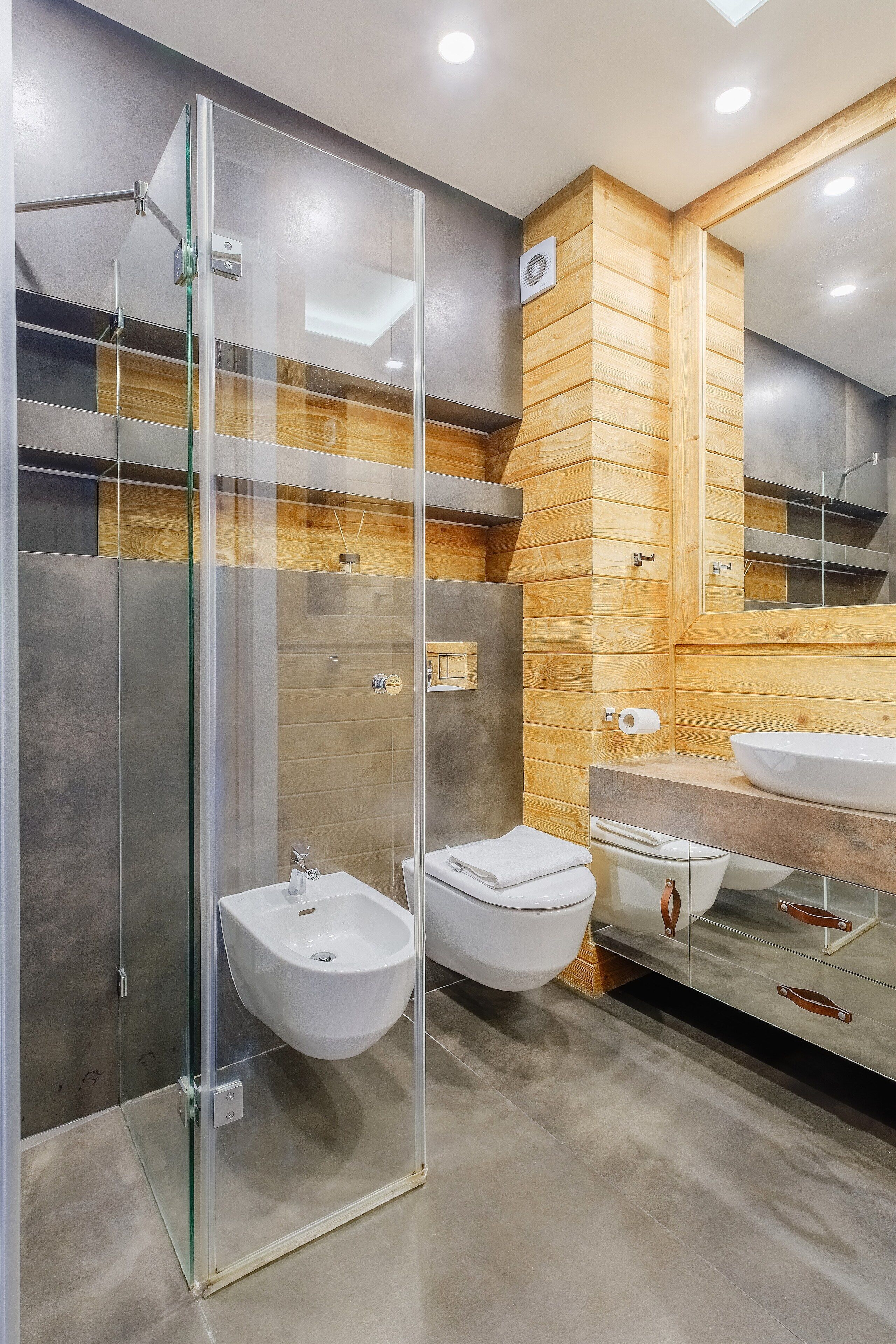 A modern bathroom with a glass-enclosed shower, two sinks, and a wooden accent wall.
