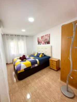 Quarto com cama, guarda-roupa de madeira, mesa de cabeceira e um quadro na parede.