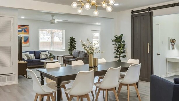 A modern dining area with a large table and white chairs, a chandelier, and a sliding door closet.