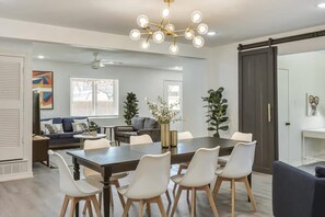 Uma área de jantar moderna com uma mesa grande, cadeiras brancas e um candelabro.