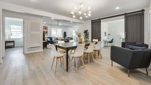A spacious living area with a dining table, chairs, a sofa, and a large window.