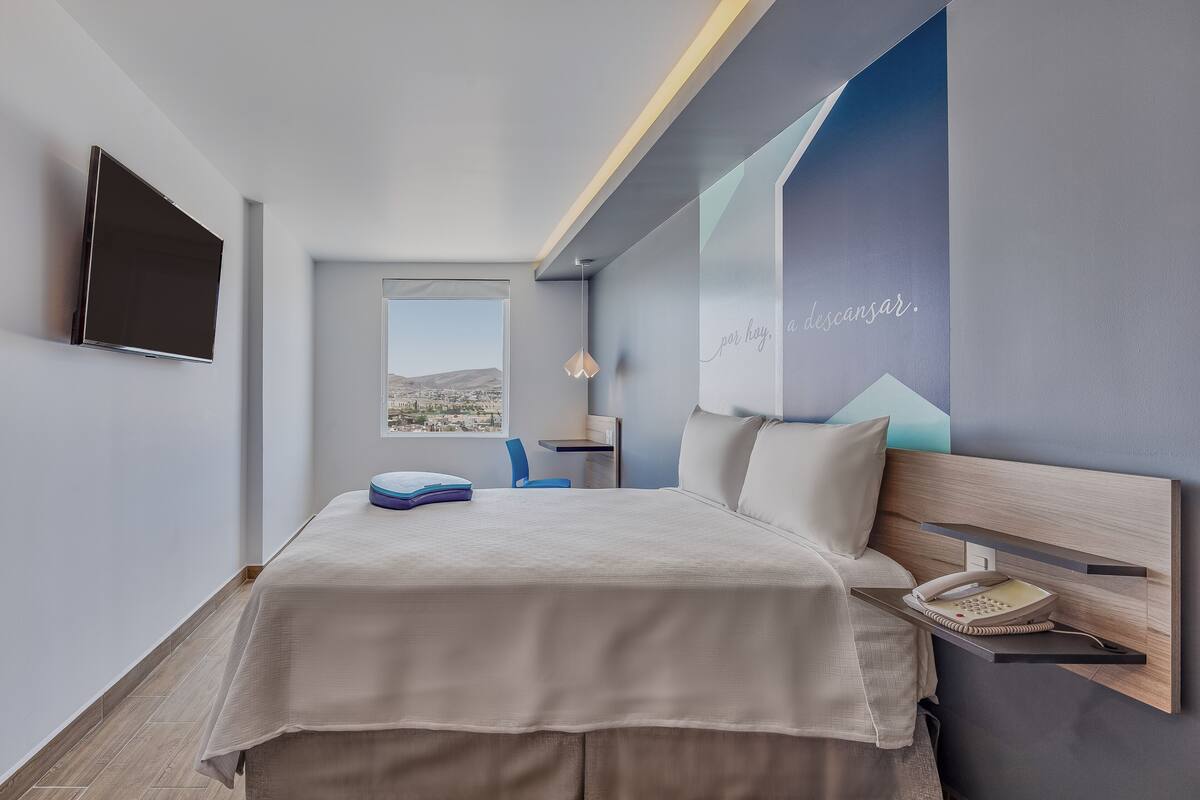 Una habitación de hotel moderna con cama, escritorio, silla, teléfono y televisión.