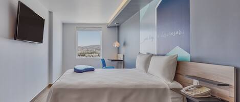 Une chambre d’hôtel moderne équipée d’un lit, d’un bureau, d’une chaise, d’un téléphone et d’une télévision.