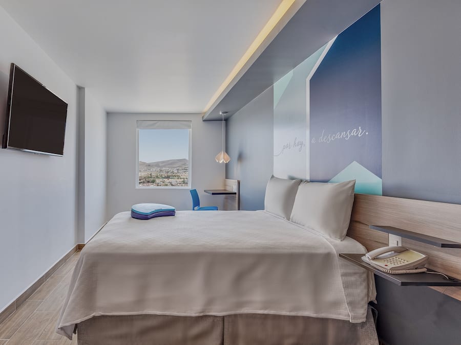 A modern hotel room with a bed, a desk, a chair, a phone, and a TV.