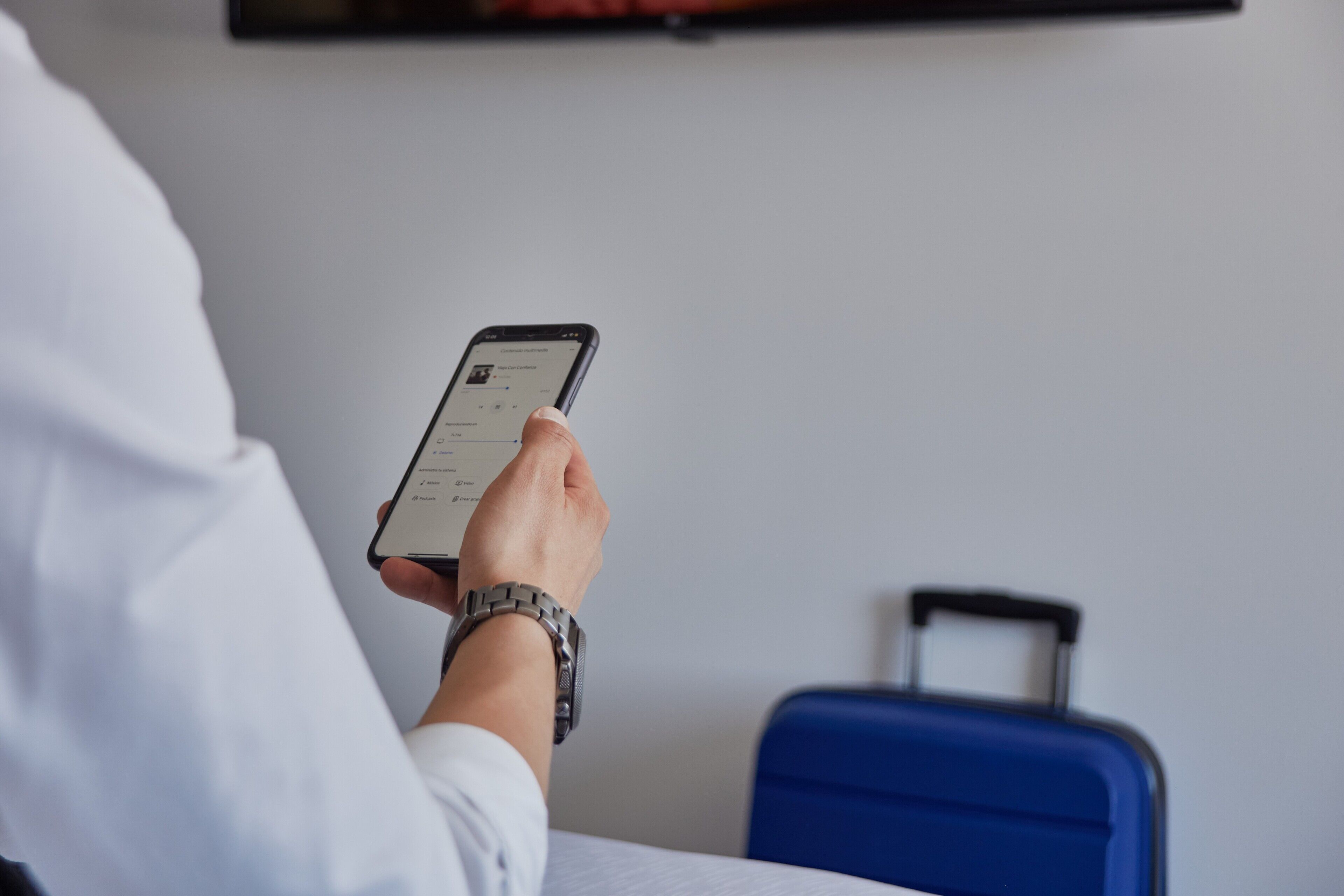 En person holder en smartphone og sidder ved siden af en blå kuffert.