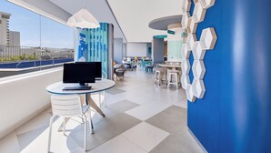 A modern hotel lobby with a large window, a round table with a laptop, and a blue accent wall. - One Mazatlán (Mazatlán)