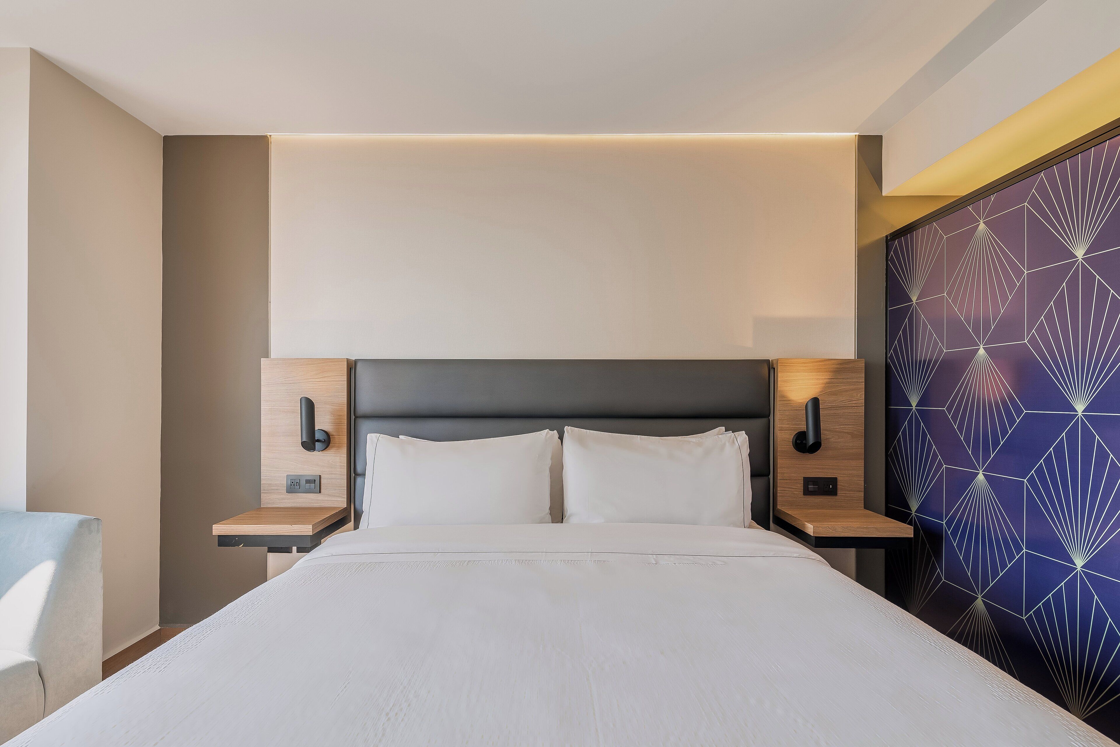 Ein modernes Hotelzimmer mit einem großen Bett, zwei Nachttischen und einer Wand mit geometrischem Muster.
