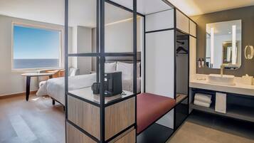 Une chambre d’hôtel moderne dotée d’un grand lit, d’un bureau, d’un coin salon, d’une salle de bain avec un miroir et offrant une vue sur la mer.