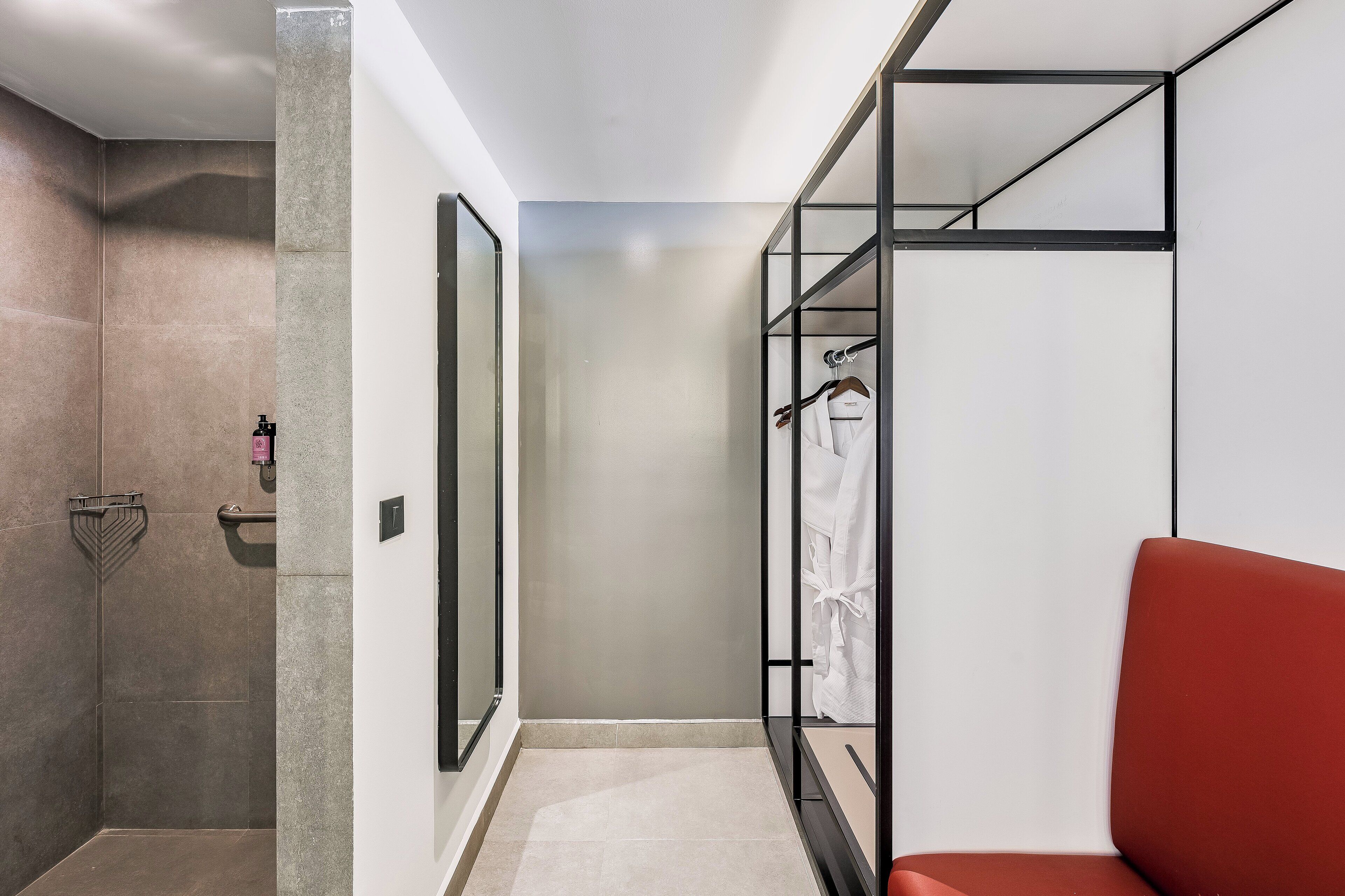 Une salle de bain moderne avec une douche, un meuble de rangement en verre et un banc rouge.