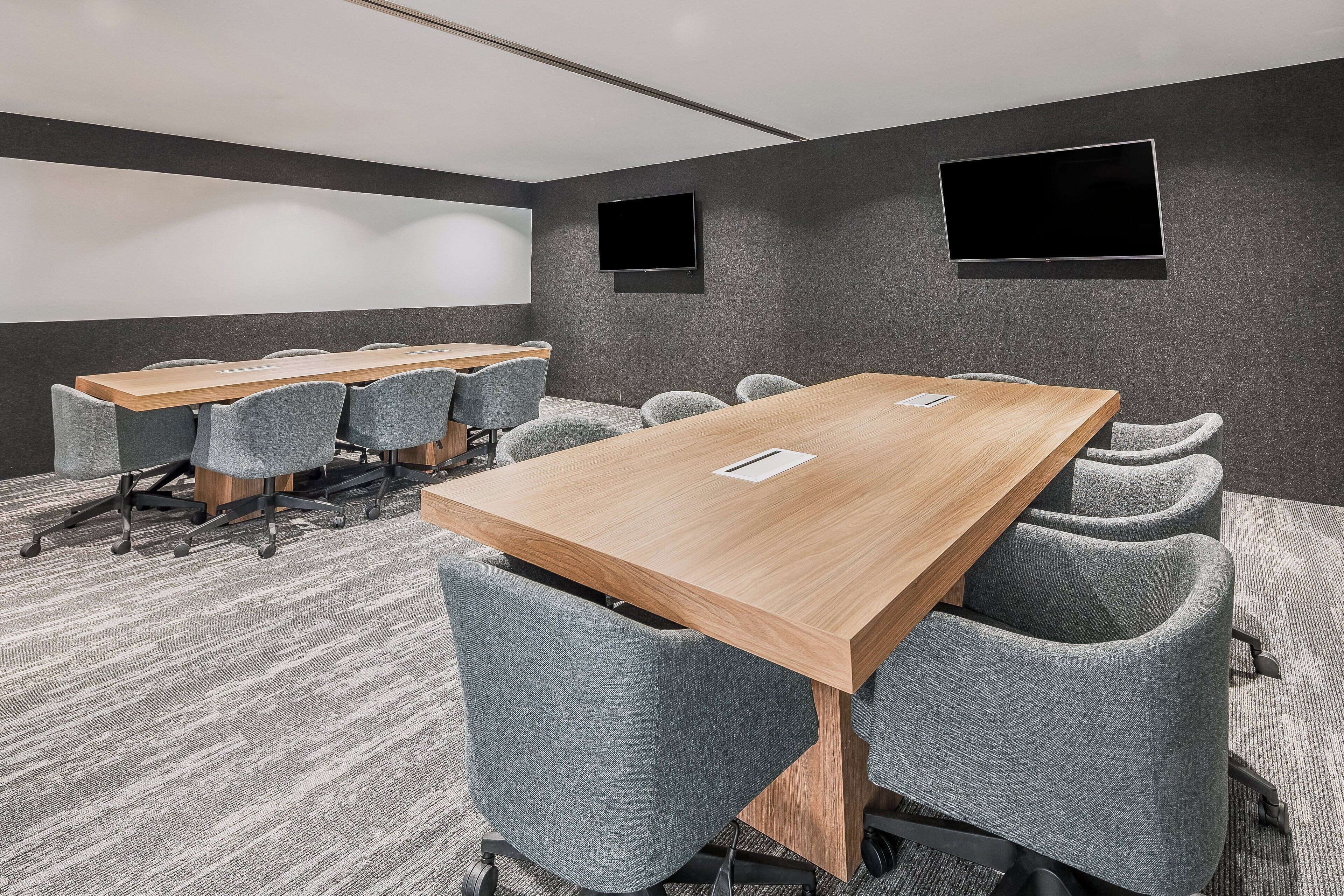 A conference room with a long table, multiple chairs, a projector screen, and a flat-screen TV.