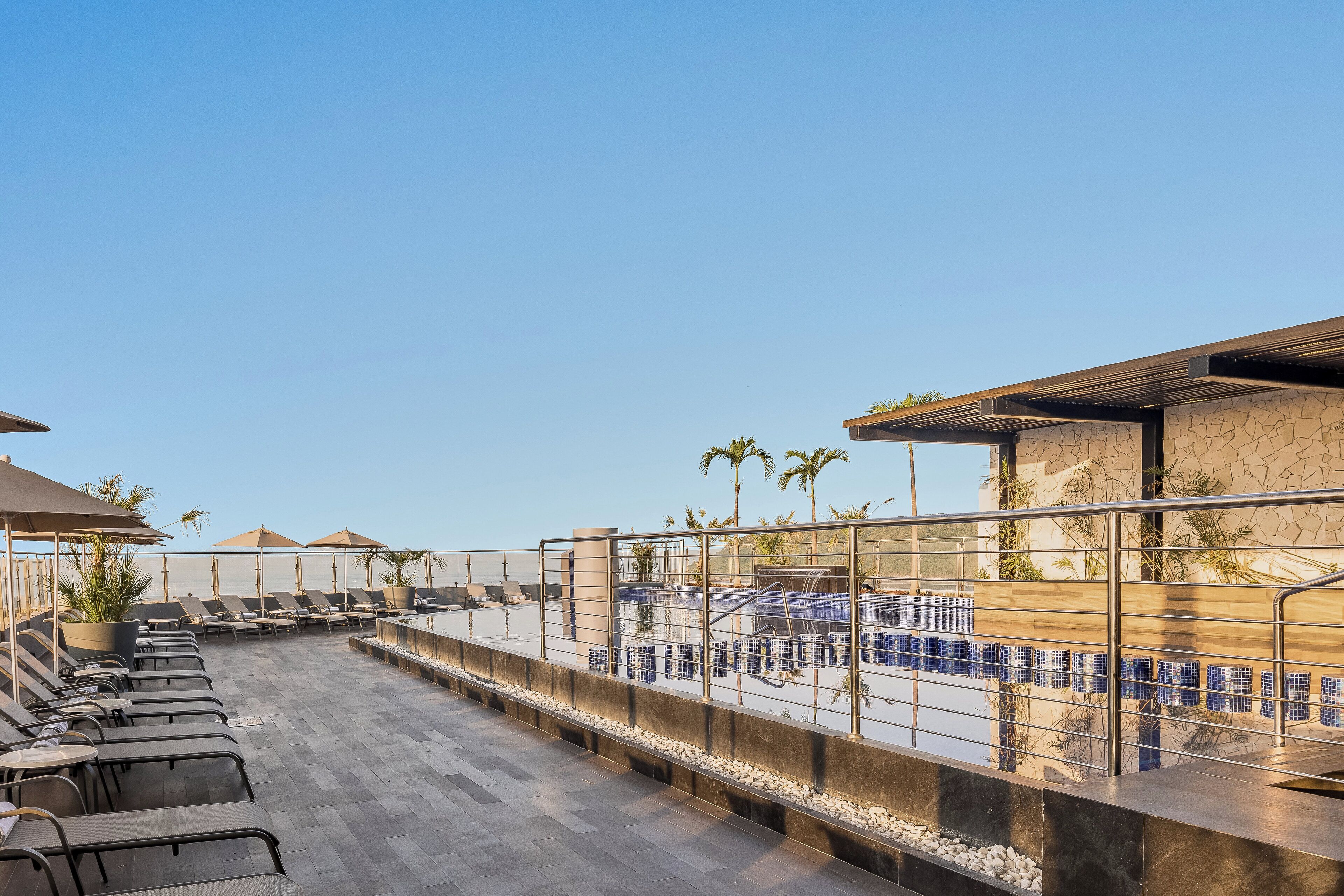 Una terraza en la azotea con sillones de descanso, sombrillas y una zona de piscina.
