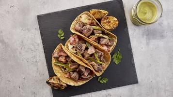 Tres tacos de carne y vegetales sobre una tabla de pizarra.