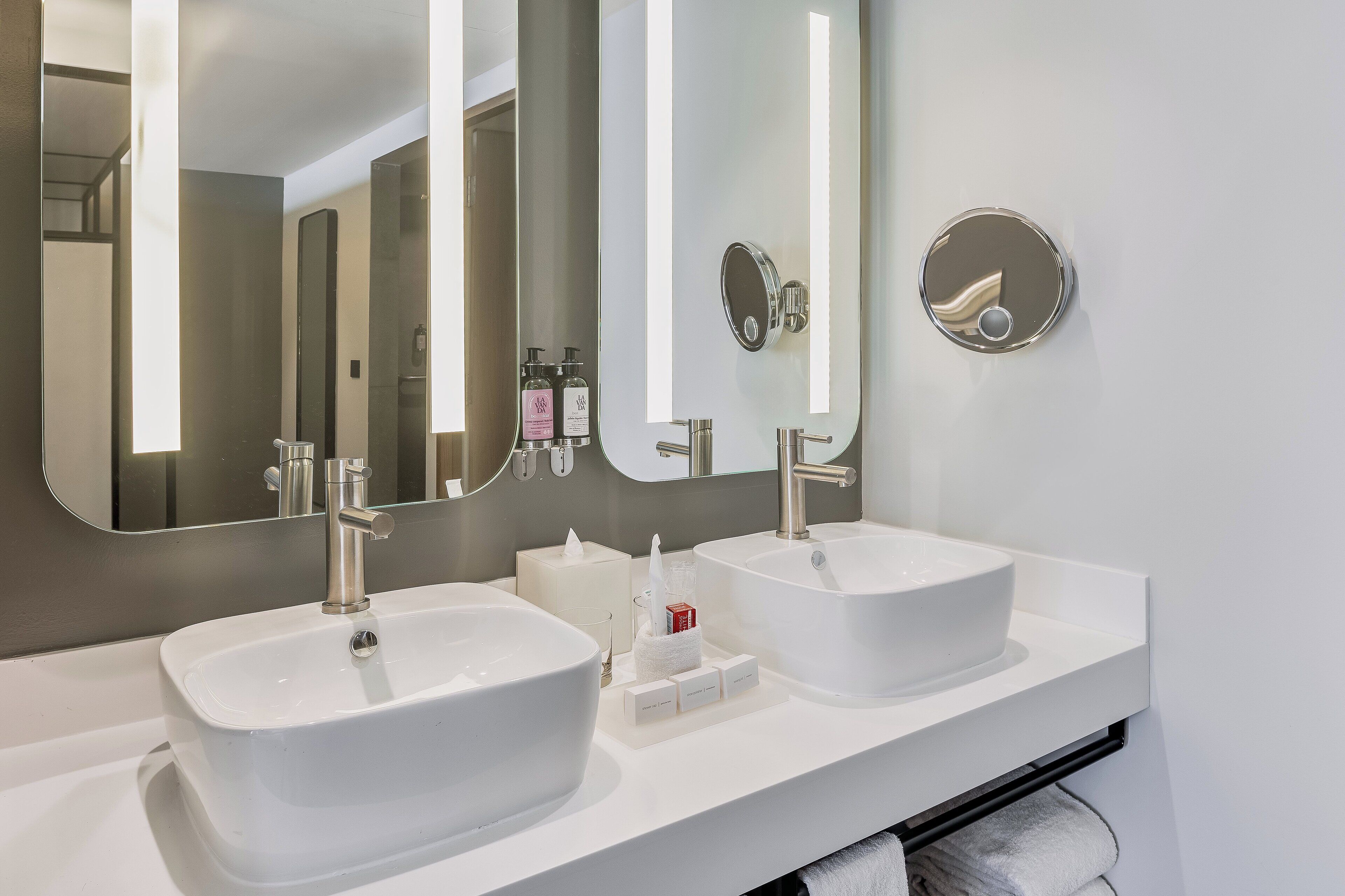 Une salle de bain moderne avec deux vasques blanches, un grand miroir et un porte-serviettes.
