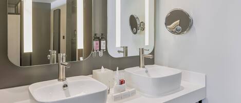 A modern bathroom with two white sinks, a large mirror, and a towel rack.
