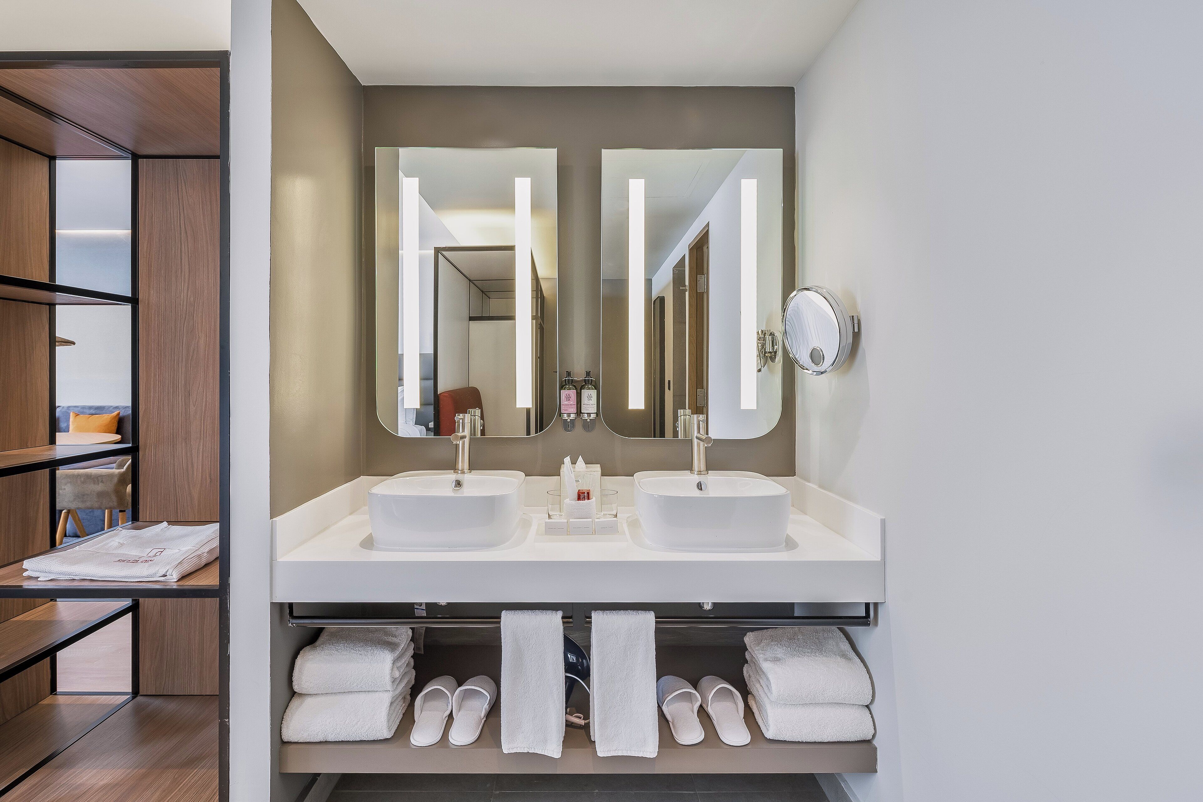 A modern bathroom with two sinks, a large mirror, and a towel rack with neatly folded towels.