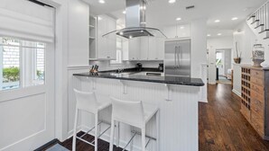 A modern kitchen with white cabinetry, a black countertop, and stainless steel appliances. There are two white bar stools at the island. - Golf Cart | 500 Yards to Beach | Bikes (Watersound)