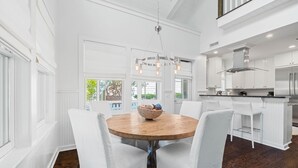 A modern kitchen with white cabinetry, a stainless steel refrigerator, and a dining area with a round wooden table and white chairs. - Golf Cart | 500 Yards to Beach | Bikes (Watersound)