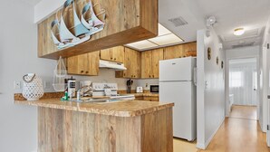 Une cuisine moderne avec des meubles en bois, un îlot central, des appareils électroménagers blancs et un luminaire au plafond qui apporte beaucoup de lumière.