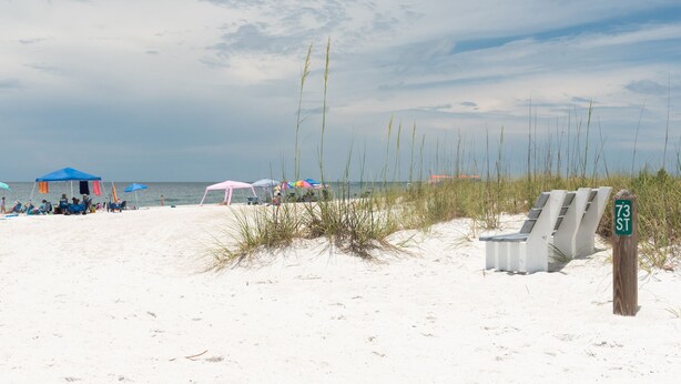 Une plage de sable blanc, avec des chaises de plage, des parasols et un panneau indiquant « 73 ST ».