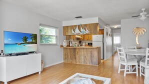 Un salon moderne avec un téléviseur, des meubles en bois et un coin repas avec des chaises blanches.