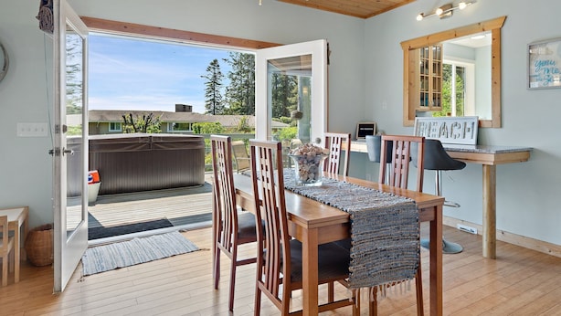 A dining area with a wooden table, chairs, and a view of the outdoors. - Seashell Cottage w/ Ocean Views, Hot Tub & Game Room: Ideal for Family & Pets (Blaine)