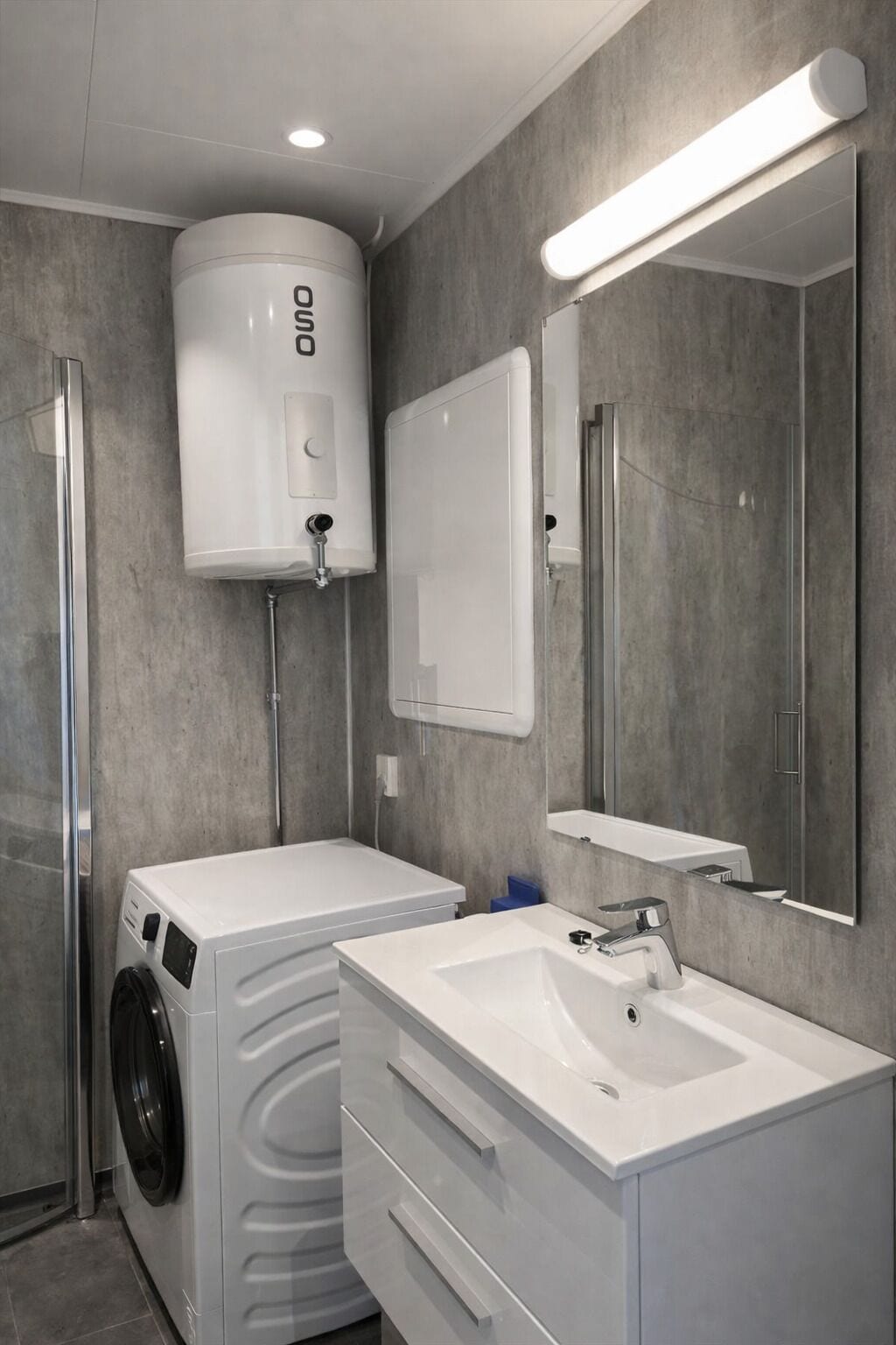 Une salle de bain moderne équipée d’un lave-linge et d’un sèche-linge intégrés, d’un lavabo, d’un miroir et de toilettes.