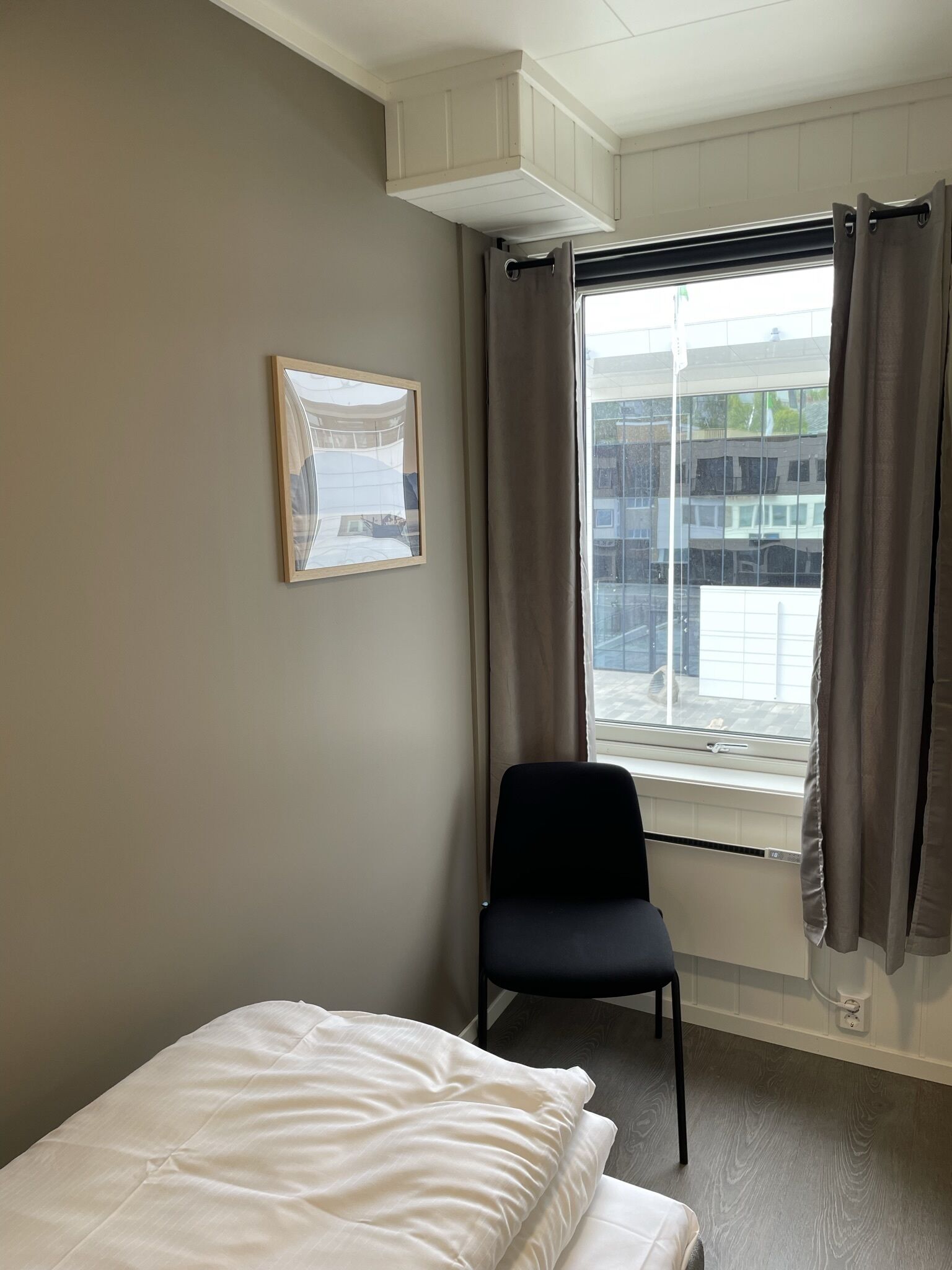 Une chambre d’hôtel avec un lit, une chaise, une fenêtre avec des rideaux et un tableau encadré au mur.