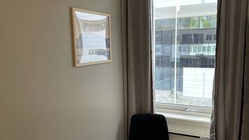 Une chambre d’hôtel avec un lit, une chaise, une fenêtre avec des rideaux et un tableau encadré au mur.