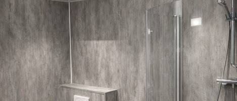 Un baño moderno con inodoro, un cubo de basura negro, cabina de ducha de vidrio y lavamanos blanco.