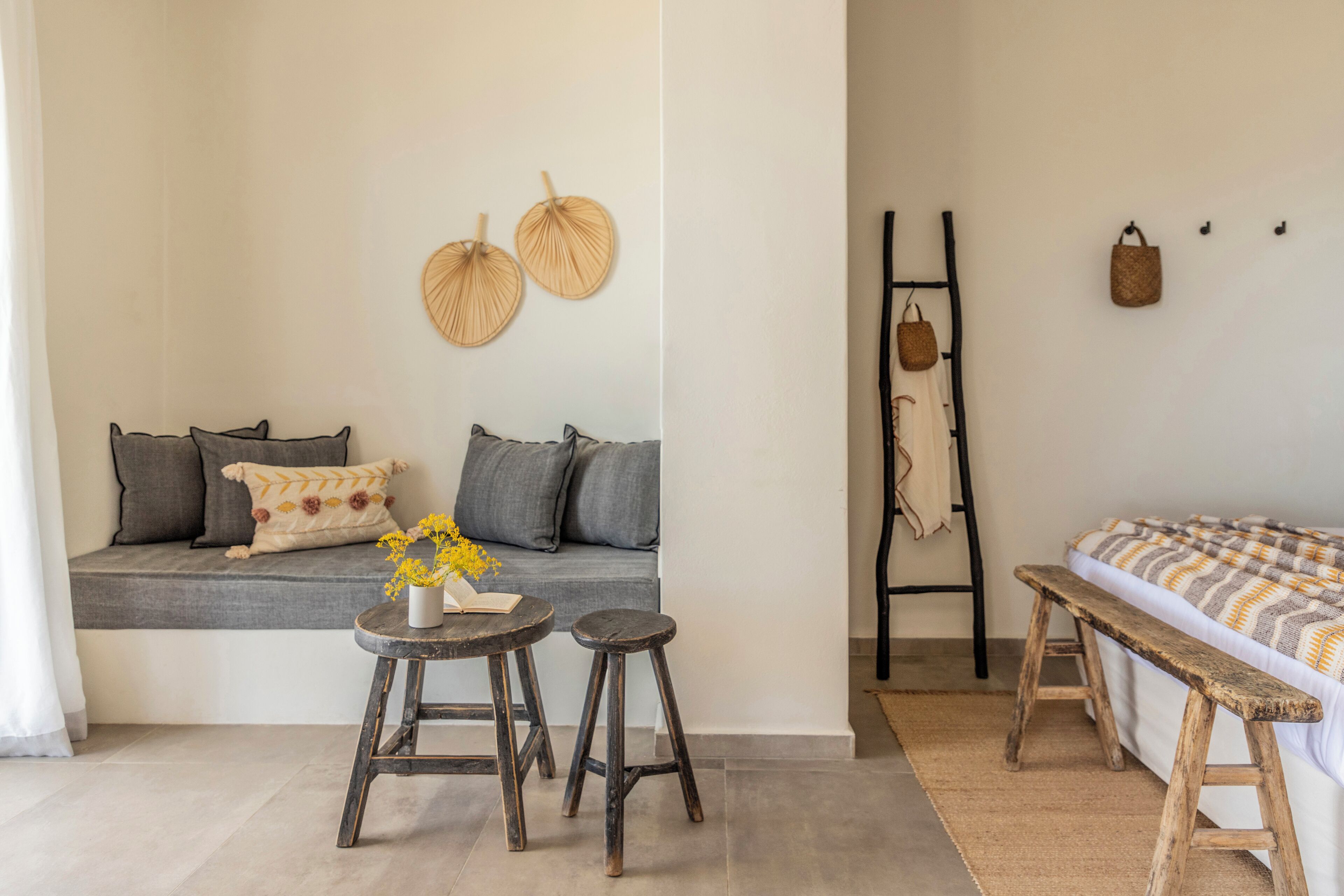 Una habitación acogedora con sofá, una mesita con un libro y flores, un banco y una cama con manta a rayas.