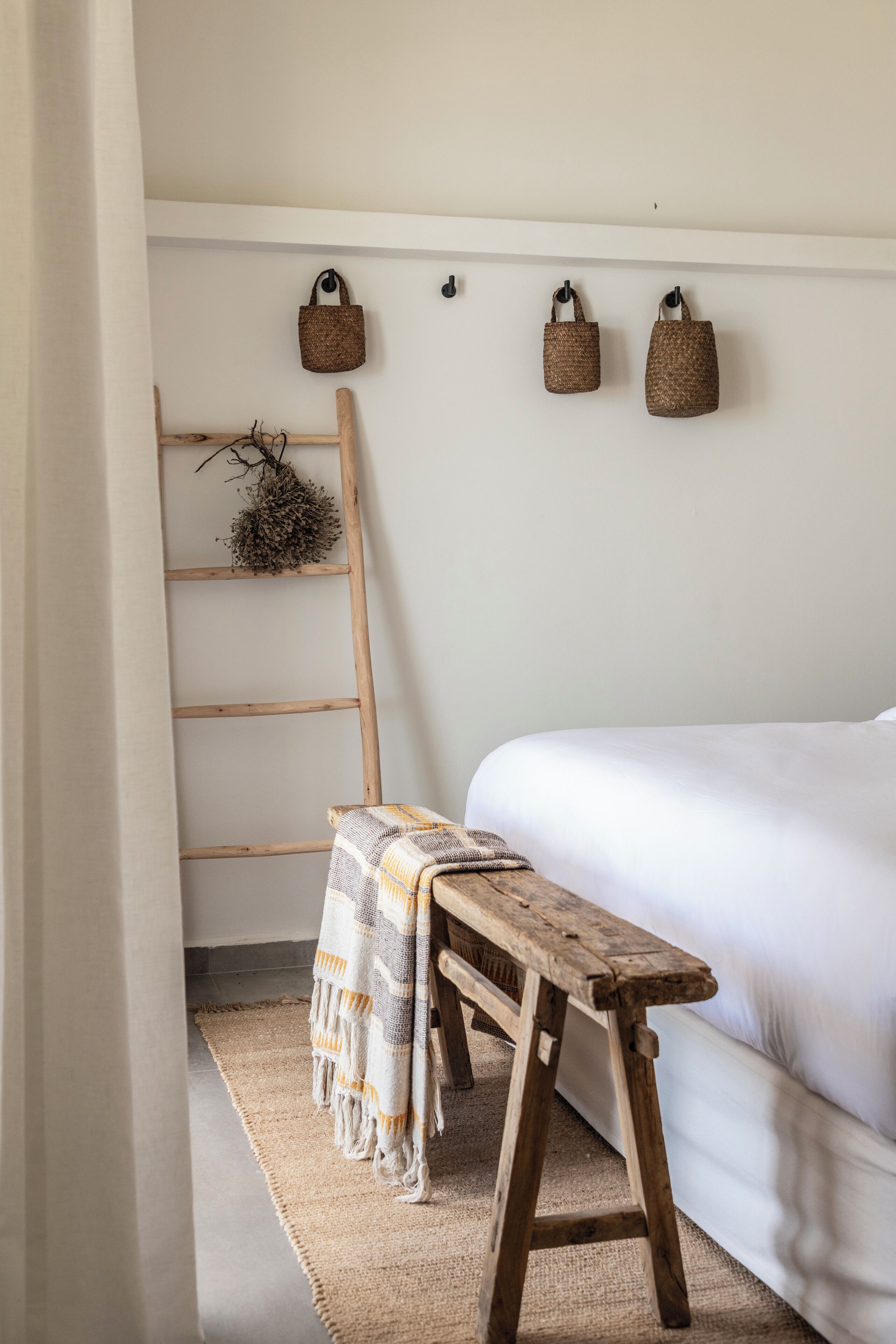A bedroom with a wooden bench, a ladder, and three woven baskets on the wall.