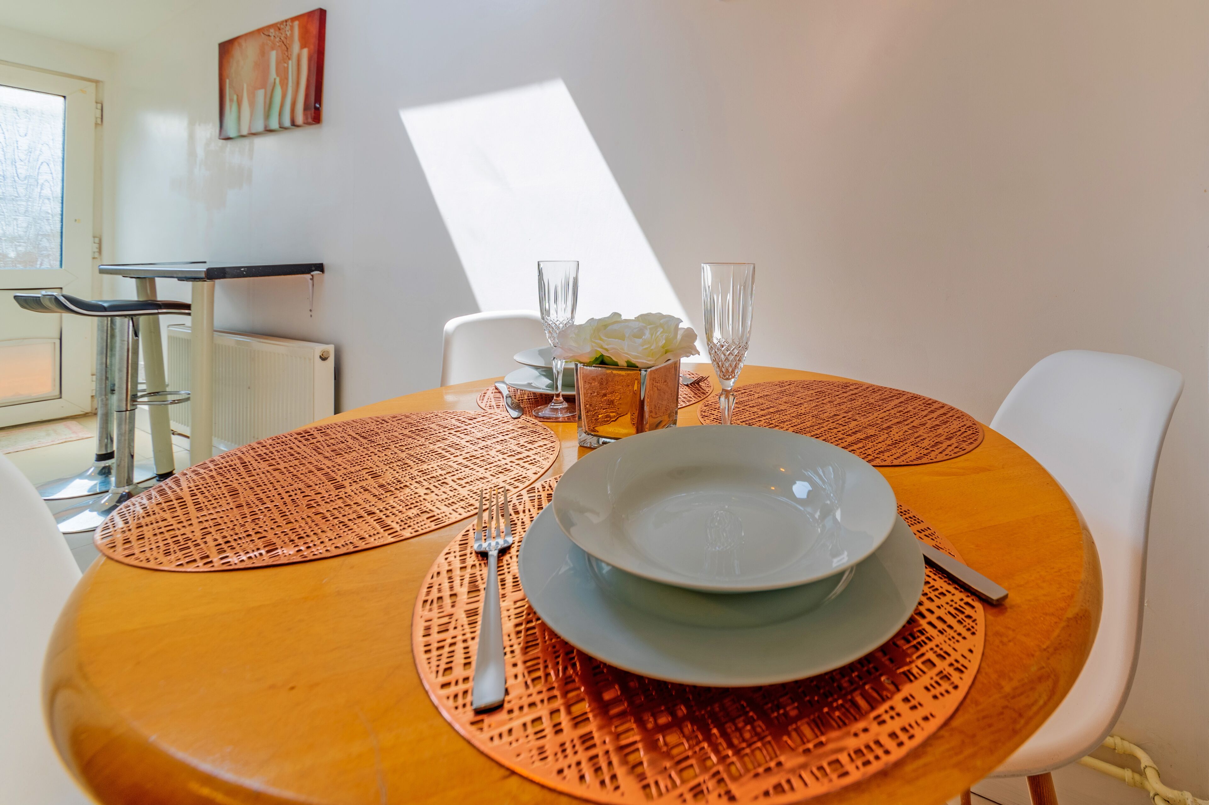 Una mesa de comedor con un posavasos de cobre, un plato blanco, una copa y un florero con flores blancas.