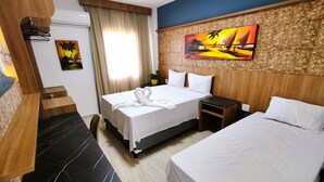 A hotel room with a bed, a nightstand, a desk, and a painting on the wall. - Apartamento 2 suítes lindo e vista mar (Fortaleza)