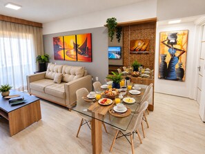 A modern living room with a glass dining table, beige sofa, and artwork on the walls.