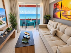 A modern living room with a sofa, a coffee table, and a view of the ocean through a glass door. - Apartamento 2 suítes lindo e vista mar (Fortaleza)
