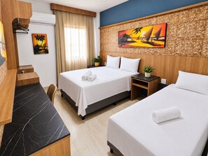 A hotel room with two beds, a desk, a chair, a painting, and a window with curtains.