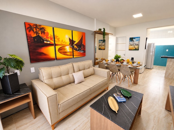 A modern living room with a beige sofa, a coffee table, and a dining area with a table set for breakfast.