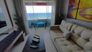 A living room with a sofa, a coffee table, and a TV. There is a balcony with a view of the sea. - Apartamento 2 suítes lindo e vista mar (Fortaleza)