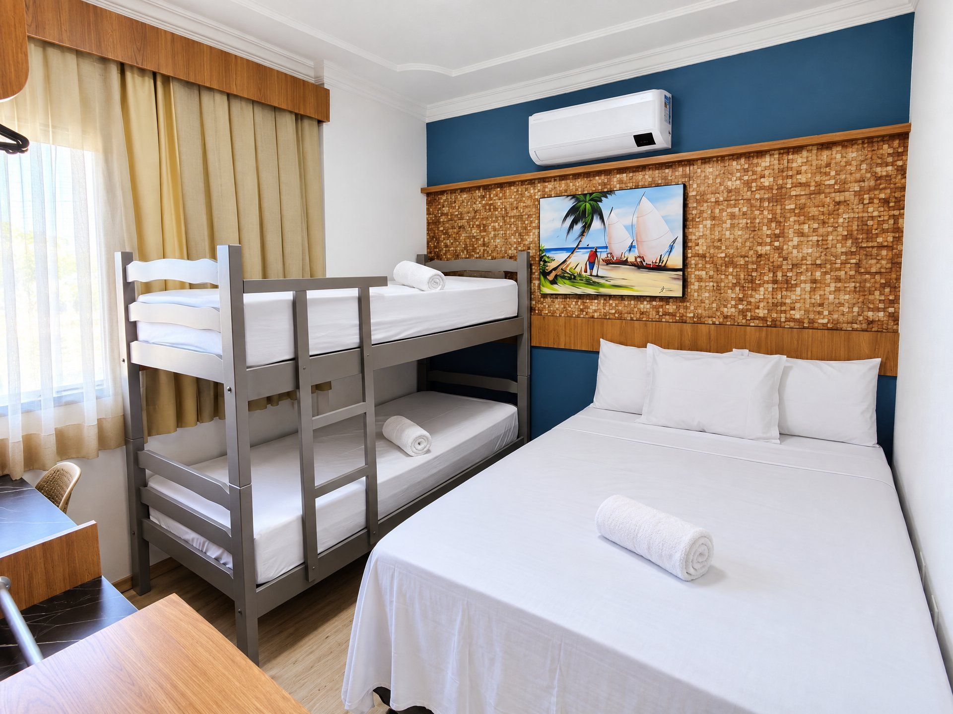 Ein Hotelzimmer mit Stockbetten, einem Einzelbett, einem Gemälde mit Strandmotiv und einer Klimaanlage.