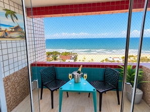 A balcony with a view of the beach, two chairs, a table, and a bottle of champagne.