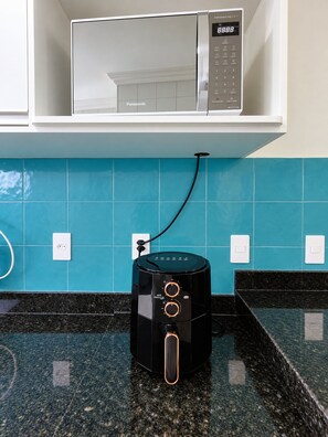 Una cucina con un forno a microonde su uno scaffale bianco, una macchina da caffè nera sul piano di lavoro e piastrelle color verde acqua sulla parete.