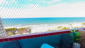 A balcony with a view of the beach, two chairs, a table, and a potted plant. - Apartamento 2 suítes lindo e vista mar (Fortaleza)