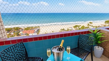 A balcony with a view of the beach, a table with a bottle of champagne, two glasses, and two chairs.
