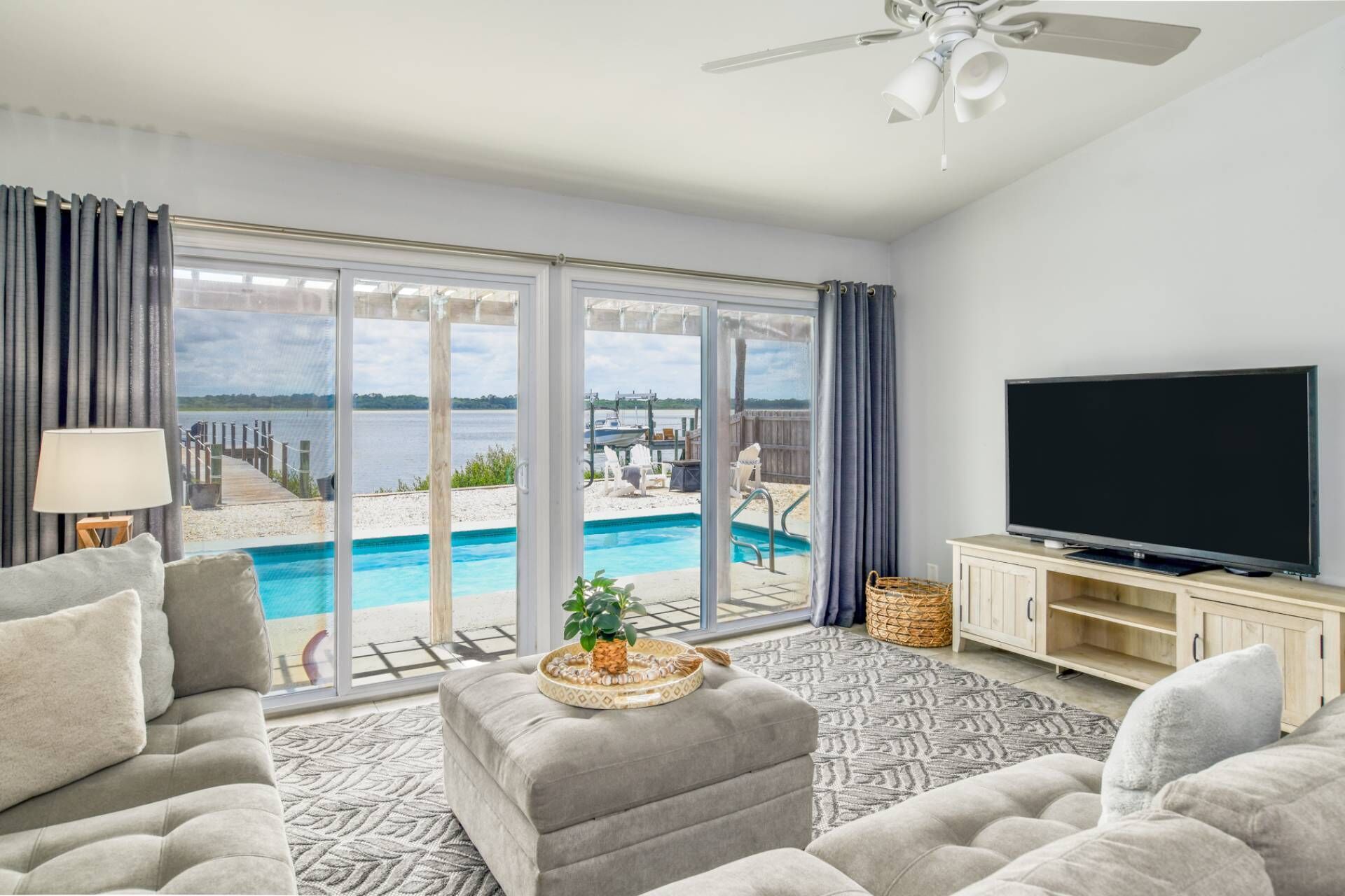 A living room with a large window, a flat-screen TV, and a pool view.