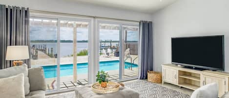 Ein Wohnzimmer mit großem Fenster, Flachbildfernseher und Blick auf den Pool.